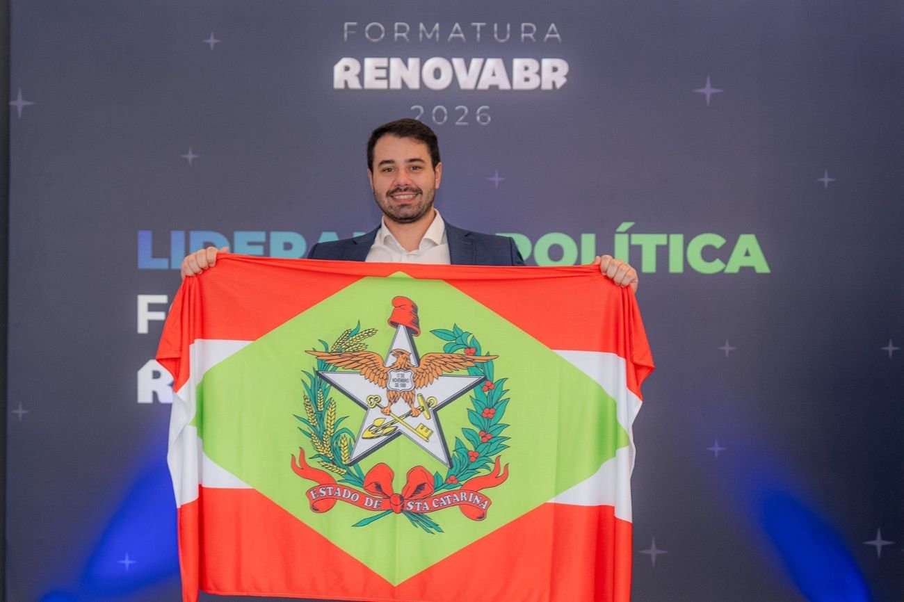 Lucas Jean segurando a bandeira de Santa Catarina diante do painel da formatura RenovaBR 2026.